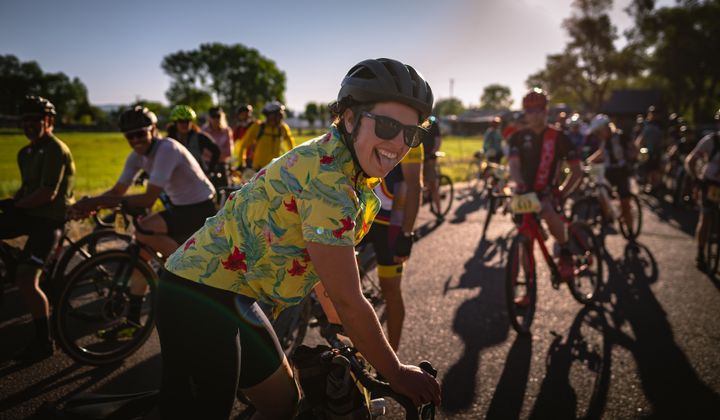 A crowd of cyclists wait for the start of a race event. Centered in the frame, a young cyclist sticks their tongue out playfully at the camera.
