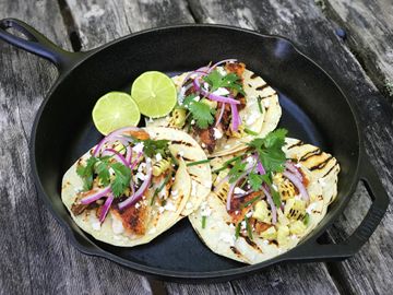 Three fish tacos arranged in an iron skillet on a table.