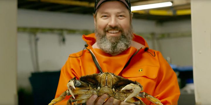 A local Oregon Coast fisherman smiles, as he presents a crab that he caught to the camera.