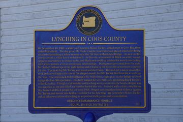 A plaque memorializing Alonzo Tucker. It reads: Lynching in Coos County. On September 18, 1902, a white mob lynched Alonzo Tucker, a Black man in Coos Bay, then called Marshfield. The day Prior, Mr. Tucker had been arrested and placed in jail after being accused of assaulting a white woman near the 7th Street Marshfield Bridge. As news of his arrest spread, a white lynch mob formed. In this era, accusations of Black-on-white assault required no evidence to arouse mobs, and Black men could be lynched for merely interacting with white women, even in consensual relationships. During transport away from the mob, Mr. Tucker fled and spent the night hiding under docks by the bay as the armed mob searched for him. The next day, Mr. Tucker was found and shot twice. The mob put a noose around his neck and carried him to the site of the alleged assault, but Mr. Tucker died from his wounds on the way. The unmasked mob still hanged his body from a light pole on the bridge in broad daylight before 300 spectators. His body hanged for several hours, prompting Black families to flee Coos Bay. Though racial hostility and lynching were prevalent in the South, Oregon was no exception to the anti-black racism that fueled this era. Founded with a state constitution that banned all Black people by law until 1926, Oregon accommodated mob violence against Mr. Tucker, and no one was held accountable for his lynching. We remember Alonzo Tucker, and all unknown victims of lynching, as we pursue truth, justice, and reconciliation. -Oregon Remembrance Project, Equal Justice Initiative