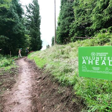 Two volunteers working on a trail behind a ‘volunteers ahead’ sign