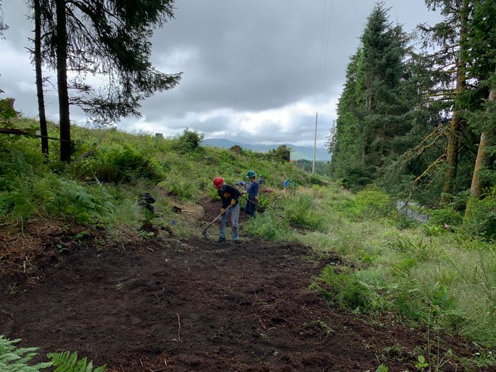 Five volunteers building a trail along a grassy hillside.