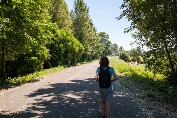A young teen, facing away from the camera, walks down a paved path.