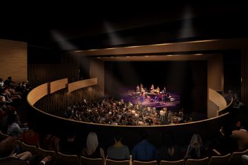 Artist’s renderingof a music performance inside the Patricia Reser Center for the Performing Arts theater. On stage, a group of musicians are performing, while a woman in a blue costume performs to the crowd. People are seated in the seats in the balcony and on the floor level, while several in the front rows are standing. 