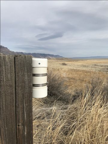 A piece of monitoring equipment is shown attached to a wooden post.