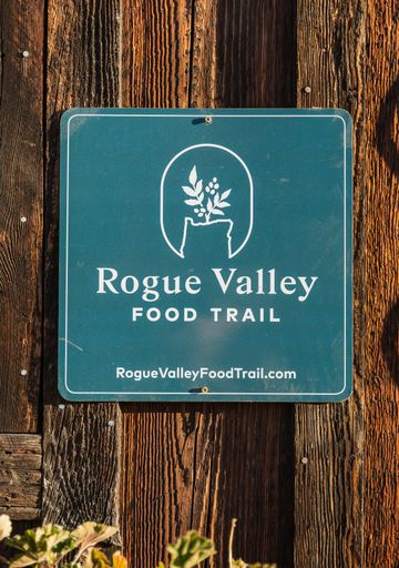 A green Rogue Valley Food Trail sign hangs on a weathered brown wooden wall at Pennington Farms.
