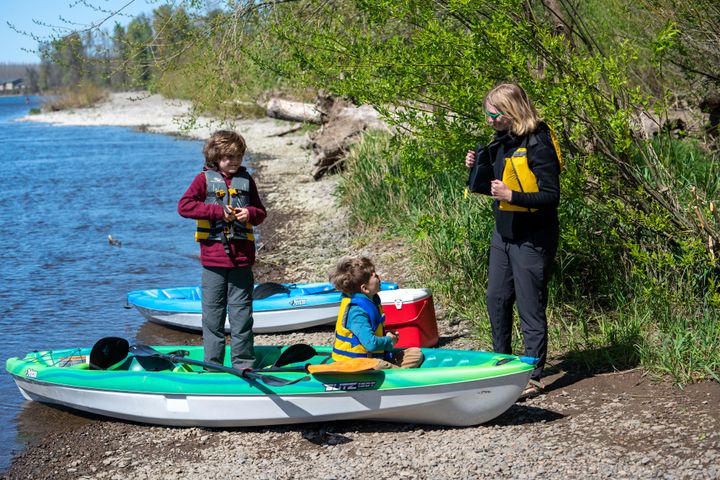 A mom and her two sons putting on life jackets before they push their kayaks out onto the river.