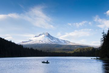Two people canoe on Trillium Lake in the Mt. Hood National Forest. A snow-covered Mt. Hood is at the center of the frame above the lake waters.