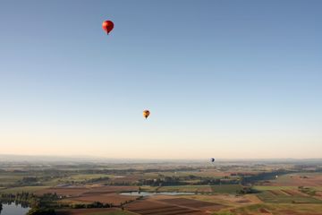 Three hot air balloons at different heights fly in a blue sky above fields in the Willamette Valley.
